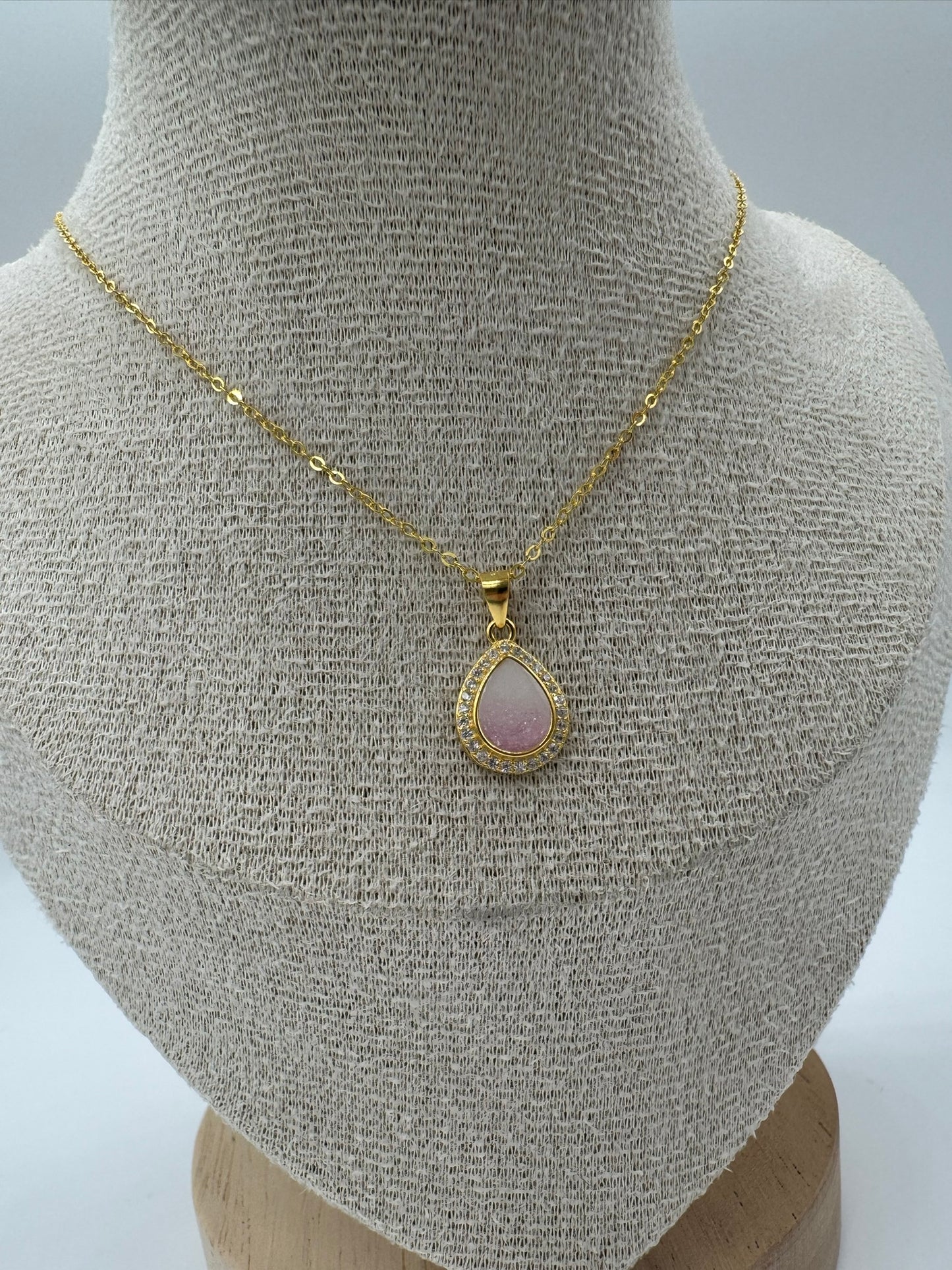 Gold necklace with a pink teardrop pendant on a mannequin bust.