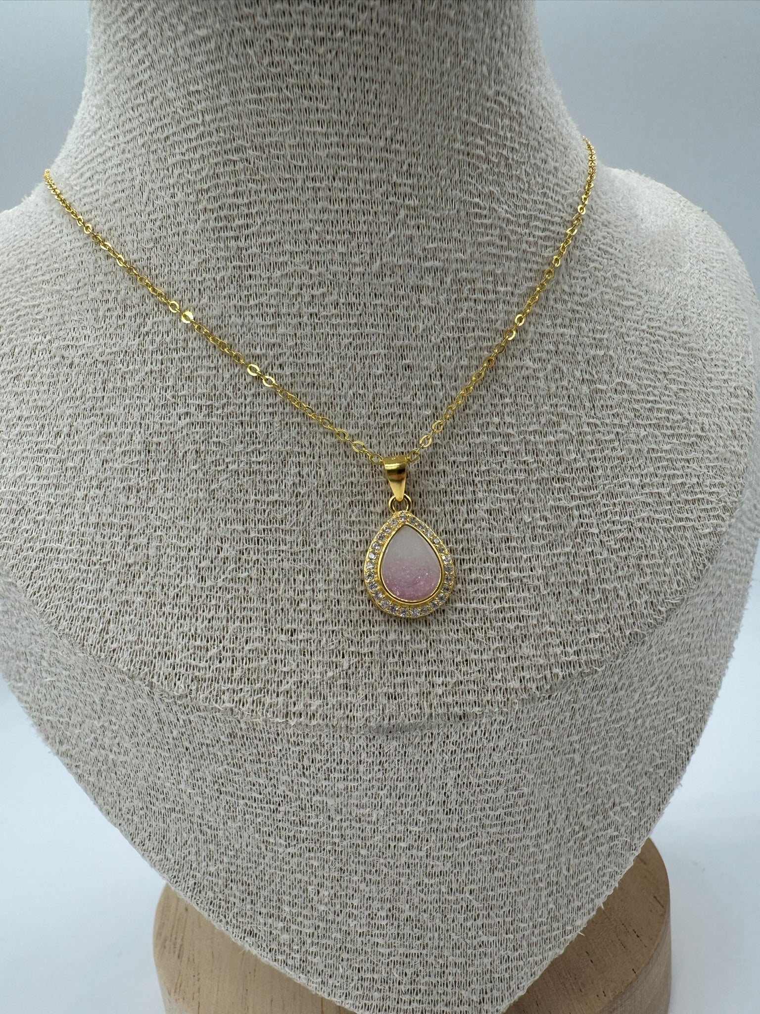 Gold necklace with a pink teardrop pendant on a mannequin bust.